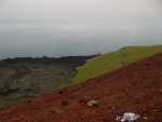 Red is the volcano crater, black is the new lava, green grass on the old lava, blue ocean, and fog rolling in.